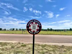 Vibrant casino shuttle bus stop sign on scenic roadside during daytime, promoting casino transportation services with QR code, ideal for travelers seeking casino shuttles and casino transportation options.